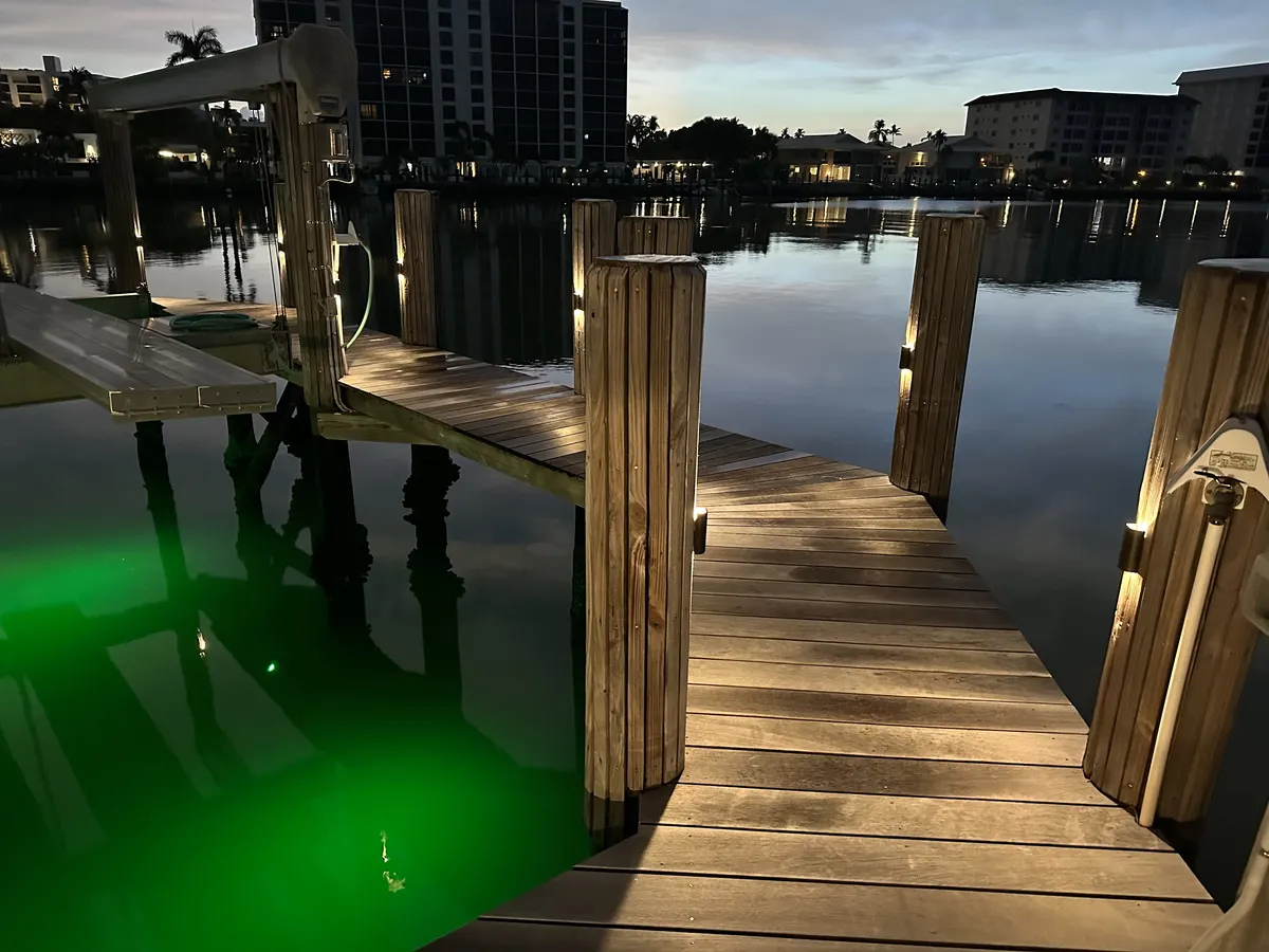 Private dock at night with underwater green lighting and lit walkway over the water