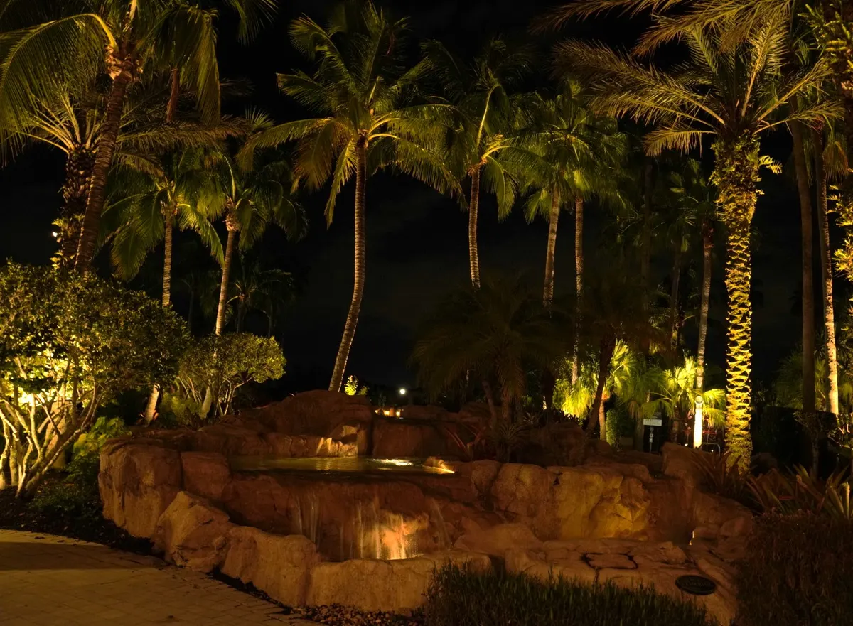 Paseo clubhouse pool area at night with illuminated palms and tiki structures