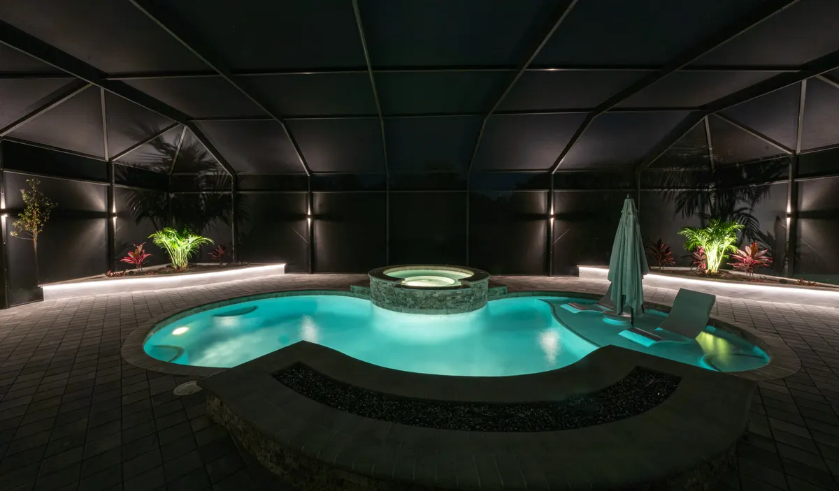 Screened lanai pool at night with soft downlighting and lit palms inside the enclosure
